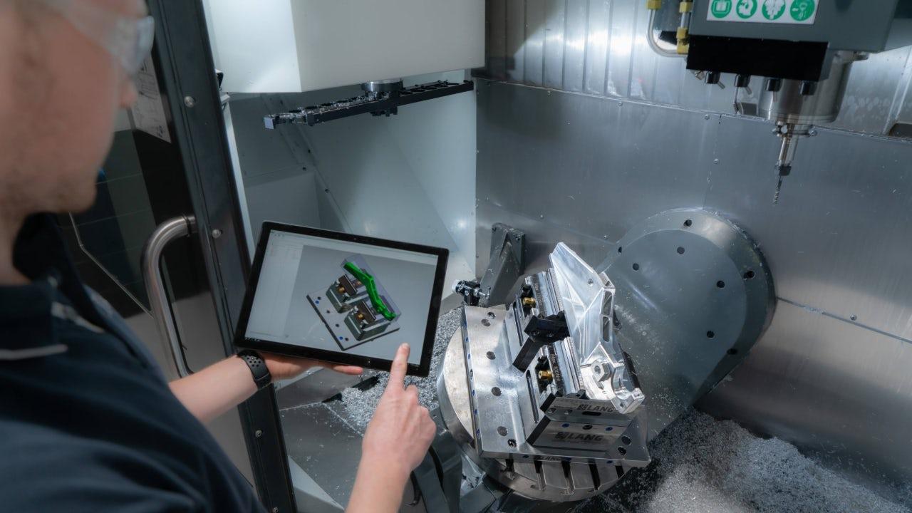 Profissional analisando projeto de fixação ao lado de máquina de usinagem